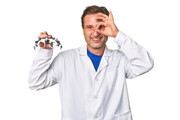 A middle-aged optometrist man excited keeping ok gesture on eye.