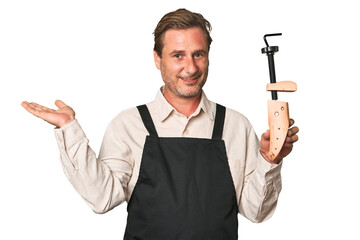 A middle-aged shoe maker showing a copy space on a palm and holding another hand on waist.