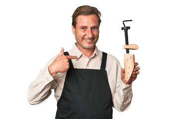 A middle-aged shoe maker person pointing by hand to a shirt copy space, proud and confident