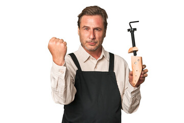 A middle-aged shoe maker showing fist to camera, aggressive facial expression.