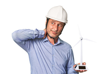 A middle-aged architect man holding a windmill model touching back of head, thinking and making a choice.