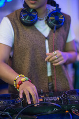 A detailed close-up shot of a DJ's hand operating a turntable, capturing the essence of a live DJ performance. The image highlights the turntable's jog wheel, knobs, and faders, with a blurred backgro