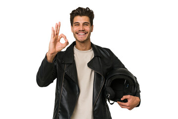Young caucasian man holding a motrbike black helmet isolated cheerful and confident showing ok...