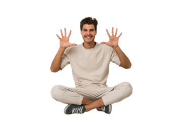 Young caucasian man sitting on the floor isolated on white background showing number ten with hands.