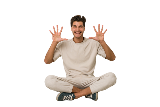 Young caucasian man sitting on the floor isolated on white background showing number ten with hands.