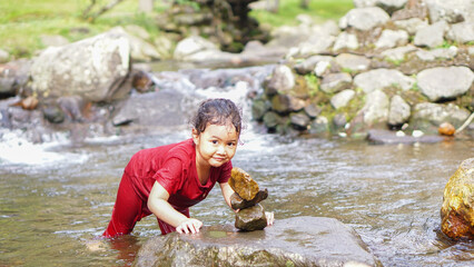 A daughter playing in a river with red clothes with stacked rocks
