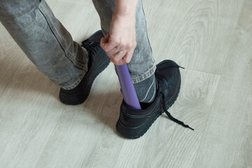 Caucasian woman putting on black sneakers using shoehorn while standing on the floor of the room.