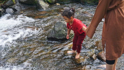 Hijab Mom and daughter playing in a river together and holding hands