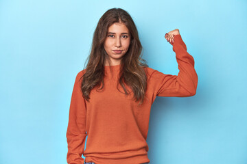 Teen girl in vibrant orange sweater on blue showing fist to camera, aggressive facial expression.
