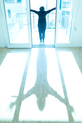 Woman Standing with Arms Outstretched on the Floor in a Empty Room with Sunlight at Home in Switzerland.
