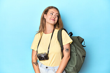 Young blonde traveler with camera and backpack in studio dreaming of achieving goals and purposes