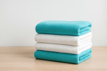 Soft folded towels stacked on wooden surface with white and turquoise colors, creating calm and clean atmosphere in minimalistic setting