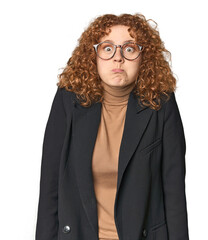 Young Caucasian redhead in business attire shrugs shoulders and open eyes confused.