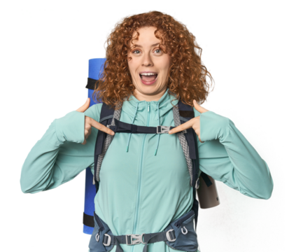 Young Caucasian redhead ready for hiking surprised pointing with finger, smiling broadly.