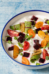 Colorful yogurt salad with grilled oranges, beets, cherry tomatoes, and greens