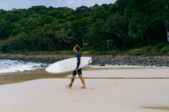 Man with surfboard walking on seashore against sky