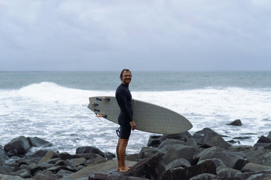 Man holding surfboard while standing on rock on beach