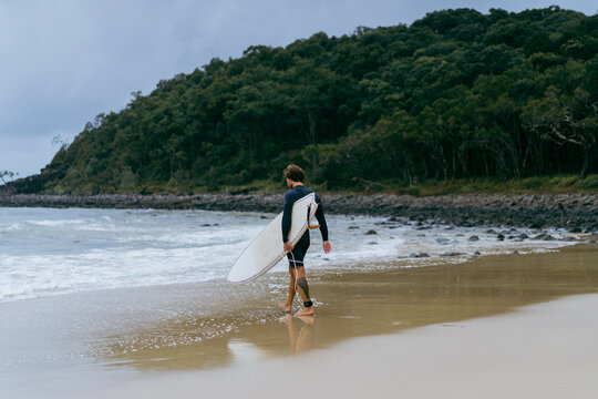 Man on beach with surfboard at sunset