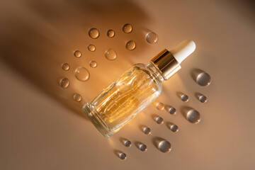 glass dropper bottle with beauty face oil 24k gold serum on beige background with shadows and serum drops. anti aging serum with natural ingredients.