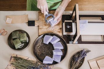 Top view of a woman refining handmade lavender soap bars surrounded by herbs and packaging...