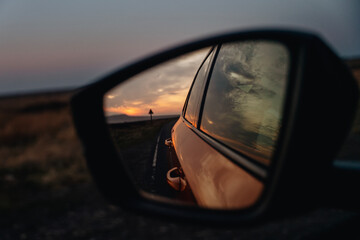 Fototapeta premium Beautiful sunset viewed in the rearview mirror while driving along a deserted road under a gentle evening sky