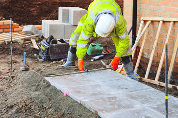 Paving works in progress as builder laying concrete paving slabs for new footpath