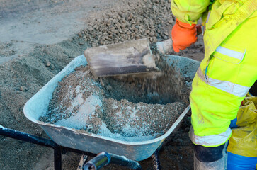 Builder mixing sand and cement mix in wheelbarrow at construction site