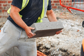 Example of manual lifting as bricklayers carrying concrete footing blocks in hand on building site