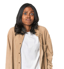 Portrait of a young Indian woman shrugs shoulders and open eyes confused.