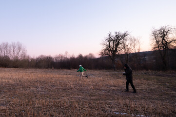 Joyful children playing in an open field during the twilight hours surrounded by trees with a...