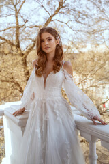 Young brunette bride in traditional long white dress posing on hotel balcony in spring