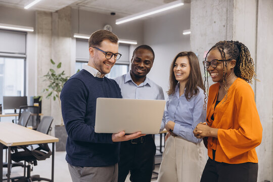 Professional team collaborating around laptop, representing workplace diversity and modern corporate interaction