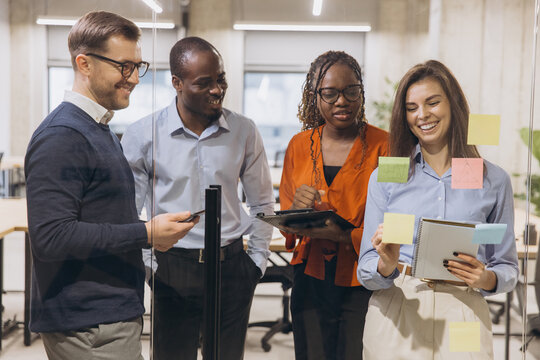 Group of diverse professionals brainstorming with sticky notes and digital devices in a contemporary office setting, showcasing teamwork and innovation