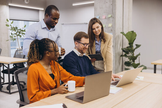Professional team brainstorming, sharing digital insights across laptops, engaging in collaborative workspace with dynamic interaction and creative energy