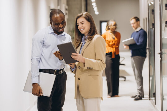Diverse team members reviewing data on tablet while walking through contemporary workspace corridor