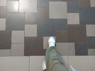 Selfie of woman legs in sneakers on the tile floor background.