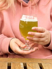 Woman in pink hoodie holding glass of matcha beer at wooden table