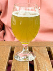 Woman in pink hoodie holding glass of matcha beer at wooden table