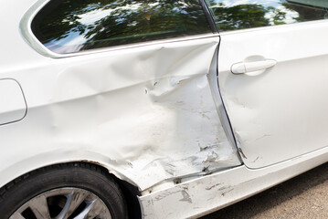 Close-up of a white car with significant side damage and dents after a collision, showing...