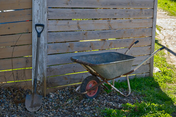 a wheelbarrow and a shovel by a wooden fence