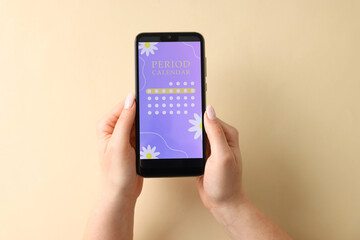 Menstruation. Woman holding smartphone with period calendar application on beige background, top view