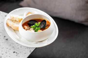 A bowl of seafood soup with mussels, garnished with fresh parsley, served alongside slices of bread on a white plate. dish is presented on stone surface, offering a cozy and gourmet dining experience.
