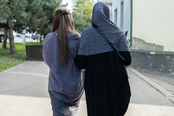 Naklejka premium Two women walking side by side along a path in a green urban area during daylight, enjoying leisurely moments together