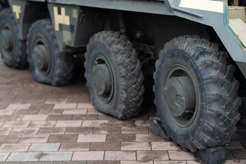 Military vehicle with flat tires parked on urban street during daylight