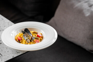 gourmet seafood pasta dish with mussels, cherry tomatoes, and creamy sauce, elegantly presented on a white plate atop a marble table. Delicious, fresh ingredients for a fine dining experience.