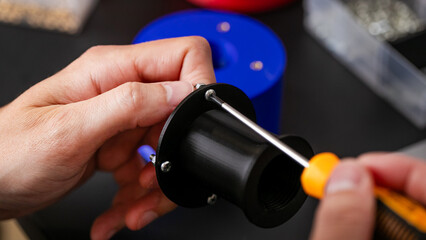 Hands of a Caucasian male assemble intricate gadget, a nod to National Inventors' Day and Tinkerfest; 3D printer, 3D printing