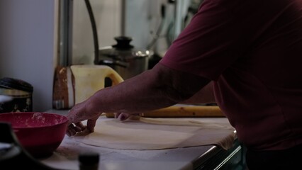 An elderly person's hands carefully stretch dough on a kitchen counter, surrounded by baking tools. This image reflects home cooking traditions, the warmth of family recipes, and the skill of handmade