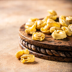 Fresh uncooked tortellini pasta on a rustic wooden board, set against a warm textured background with copy space. Healthy Italian food concept