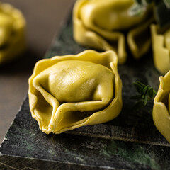Close-up of fresh uncooked tortellini pasta on a dark textured surface, garnished with fresh herbs for a rustic presentation.