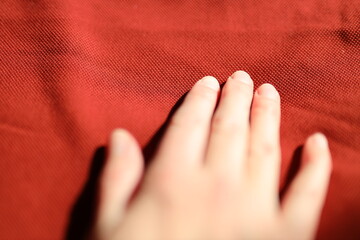 A hand is touching a red fabric. The hand is the main focus of the image, and the red fabric is the...